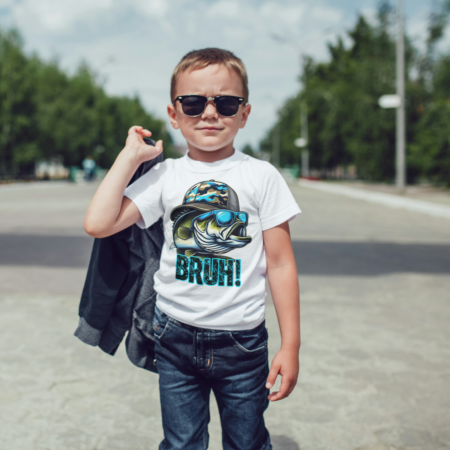 Child wearing a white t-shirt with a graphic design and text, standing outdoors on a road.